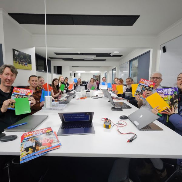 Educators sit at a desk in the Engineering precinct, holding their information booklets, smiling