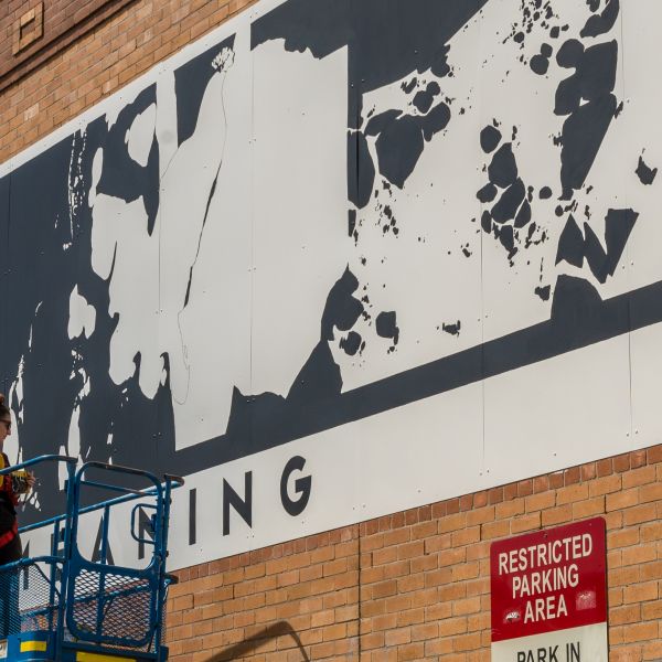 Large black and white mural on brick wall painted by artist on scissor lift