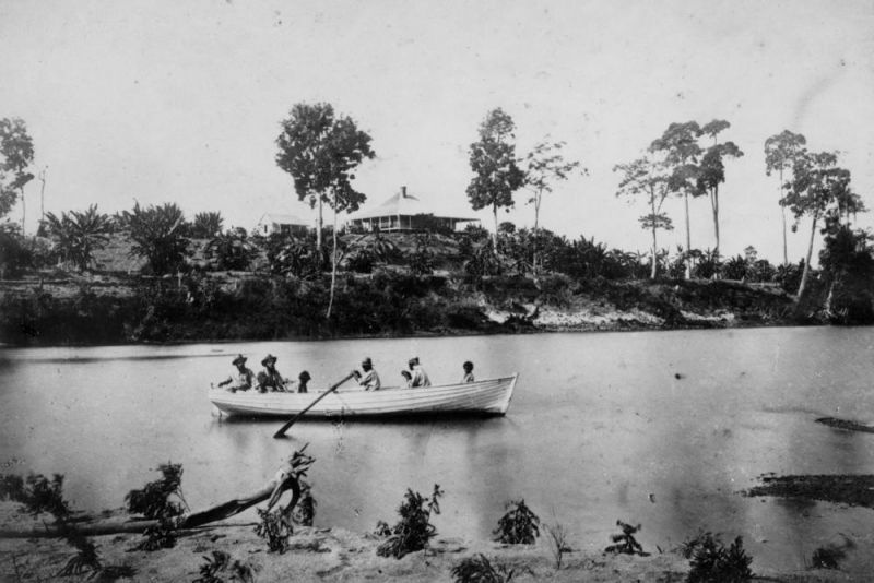 Men sitting in a rowboat on the water, a house on a hill in the background