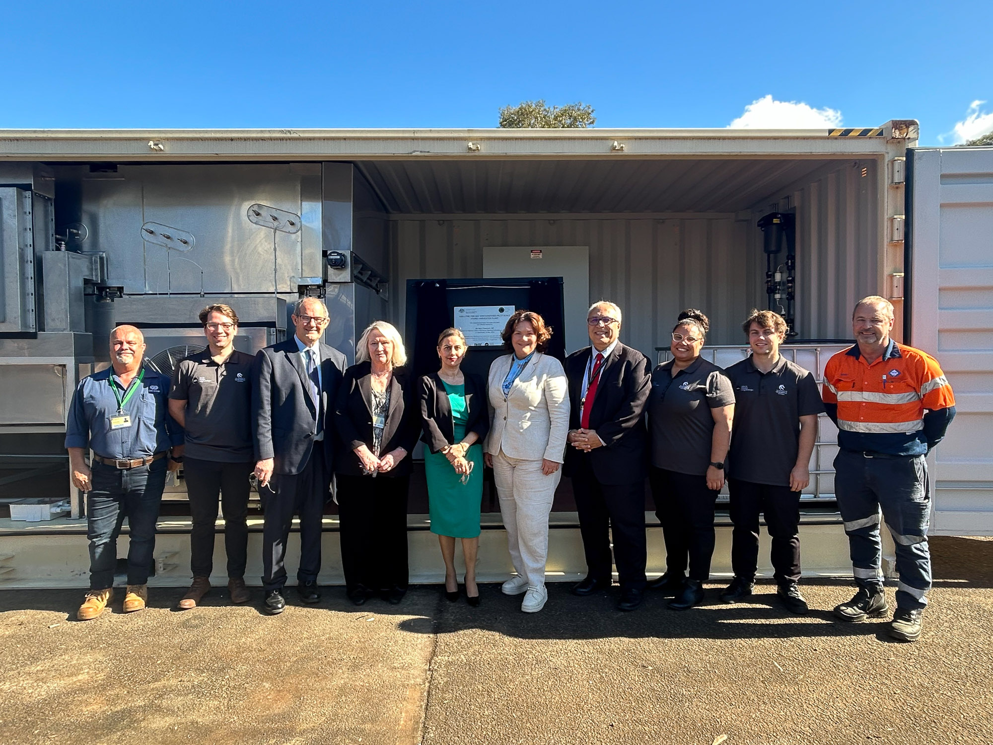 Group shot of 10 people including the Hydro Harvester team with VIP guests, standing in front of the Hydro Harvester, outdoors