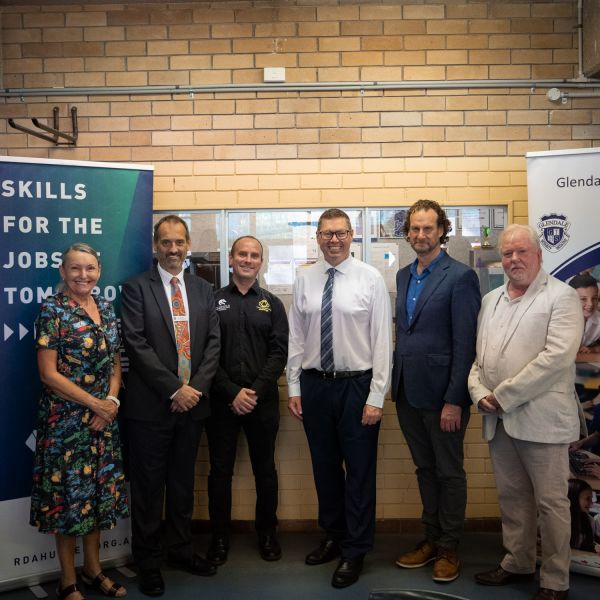 A group standing smiling at the camera with a branded banner backdrop . $1.9m funding boost for the Next Gen STEM program in schools