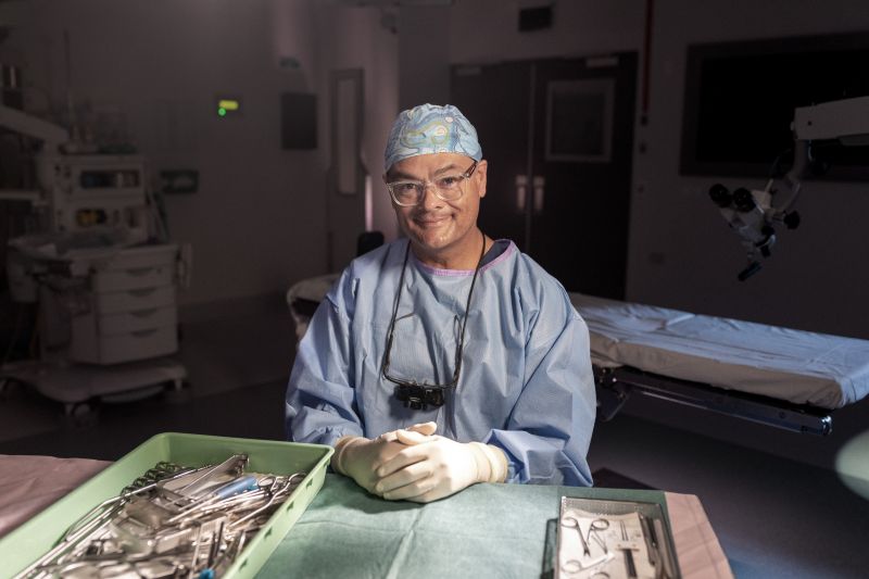 A man sitting in lab and wearing scrubs, smiling