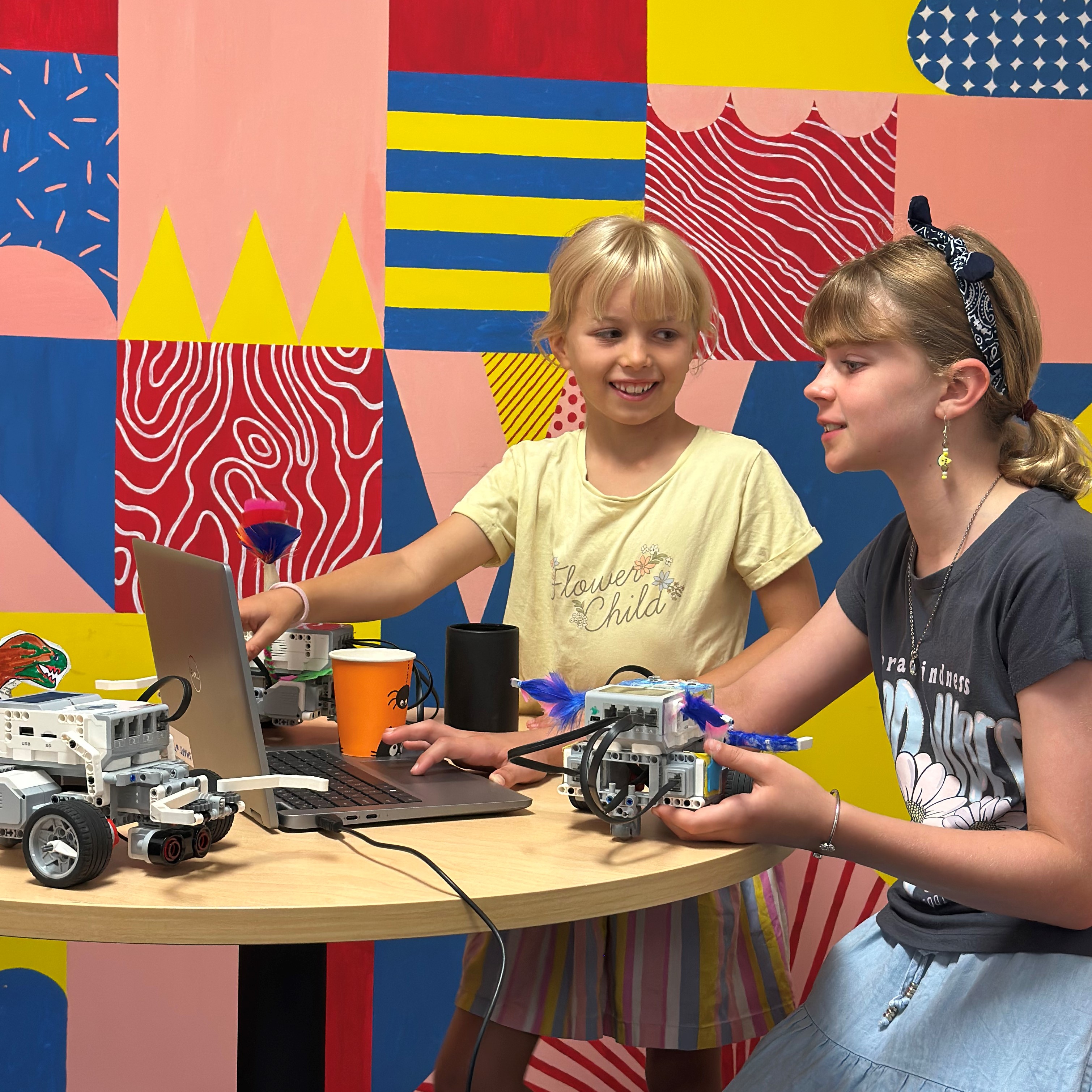 2 girls holding a robot and pointing to a computer