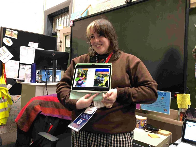 Young woman in a classroom showing a class a tablet with pictures of her nature diary