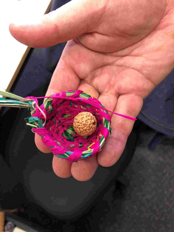 A tiny brightly coloured woven basket in someone's hand
