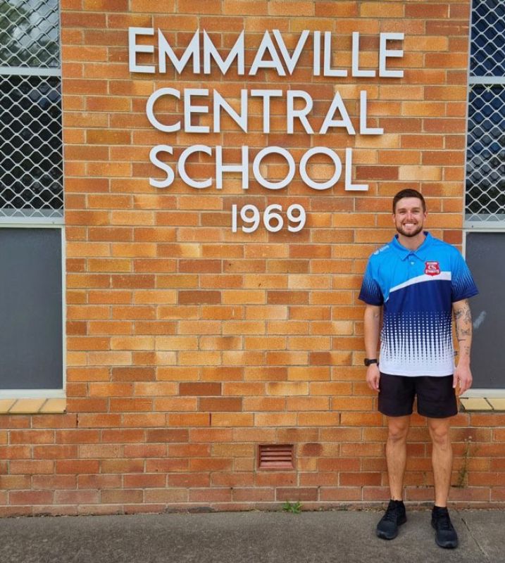 Josh is standing in front of a sign that reads 'Emmaville Central School 1969'.