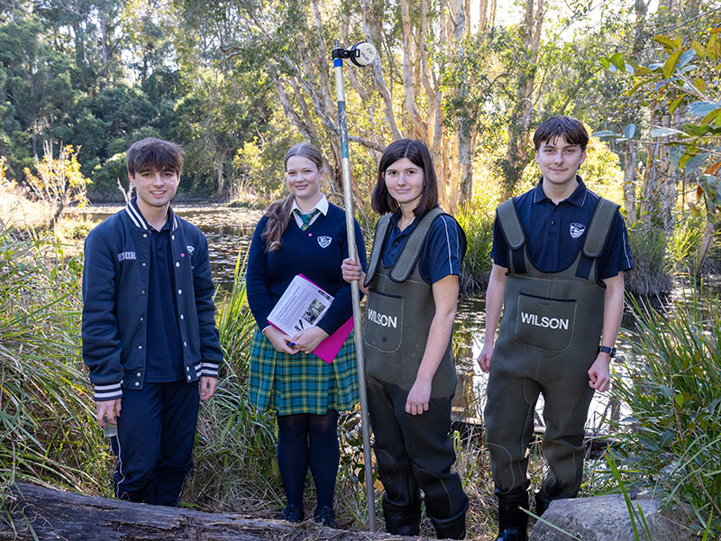 Students pose with equipment in front of a pond