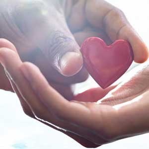 Image of two hands, with one handing a red heart into the other
