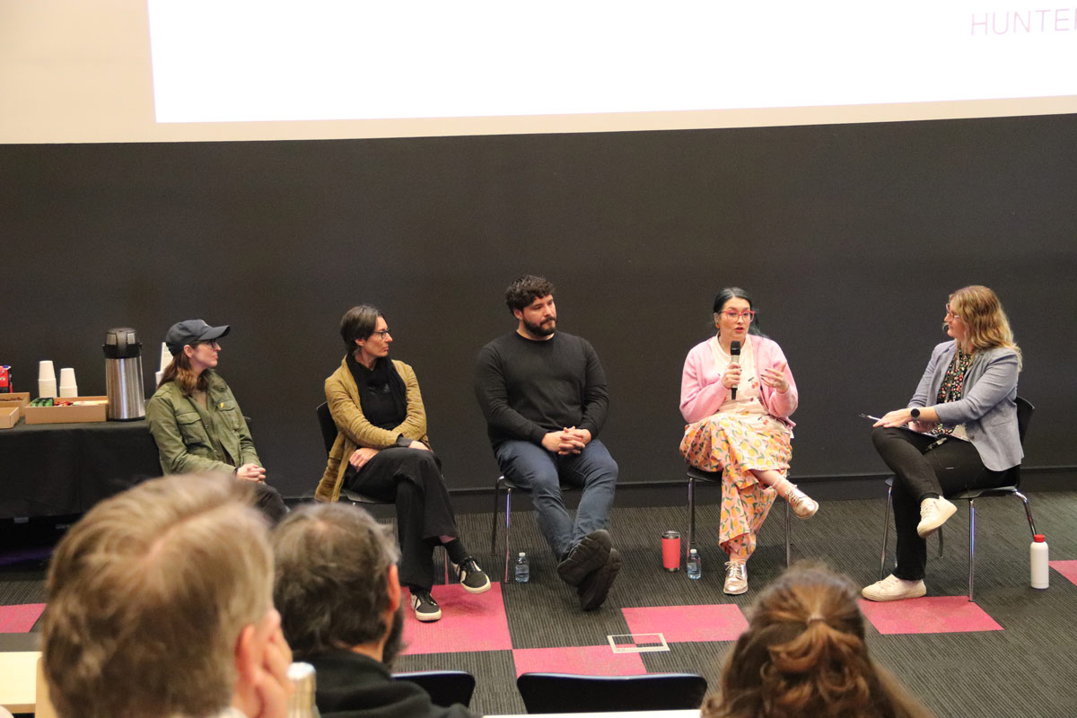 Five panalists sitting on stools on stage in front of audience