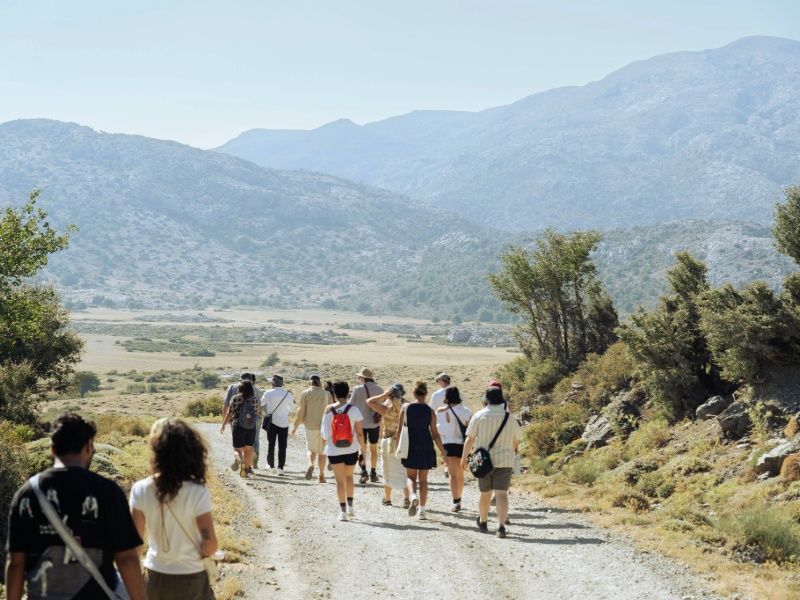 A diverse group of people walking together on a dirt road surrounded by greenery.