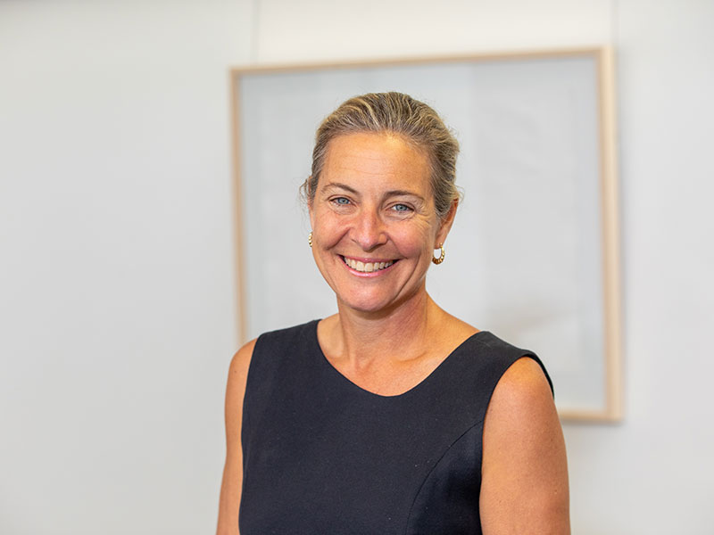 Professor Jennifer Milam smiling, wearing black blouse, hair pulled back in front of white wall  