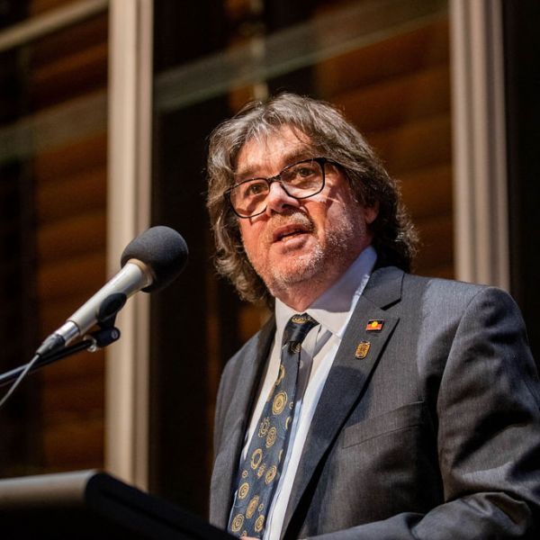 Close up of Professor Maynard dressed in a suit, standing at a lecturn and speaking into a microphone. Academy membership great source of pride