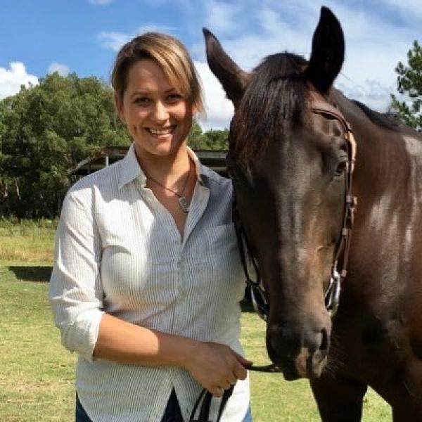 A woman stands next to a brown horse looking at the camera