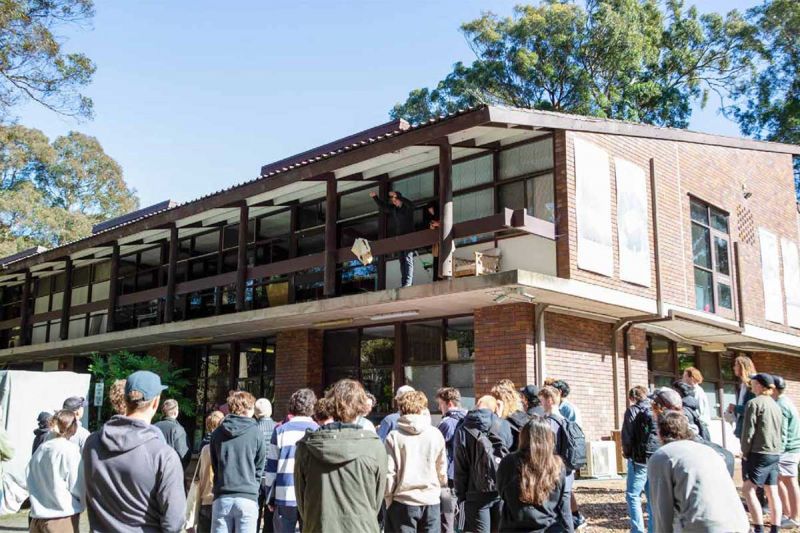 A group of students gathered beneath a balcony where the egg drop challenge is taking place