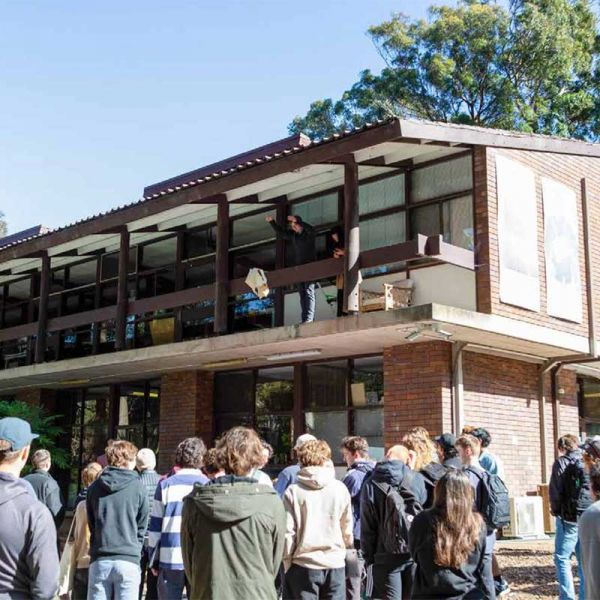 A group of students gathered beneath a balcony where the egg drop challenge is taking place