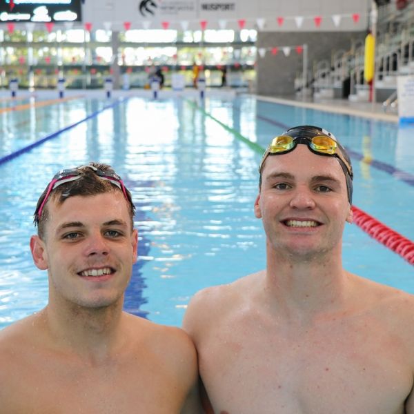 Two male swimmers in a pool standing and smiling