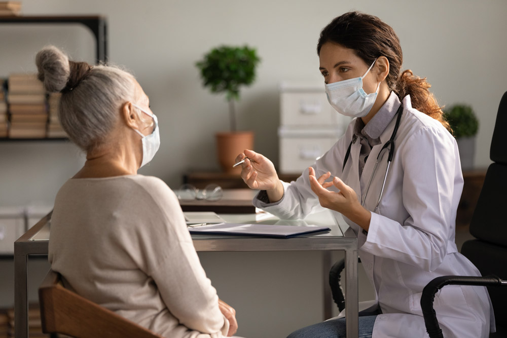 A doctor wearing a mask seeing a female patient in their office.