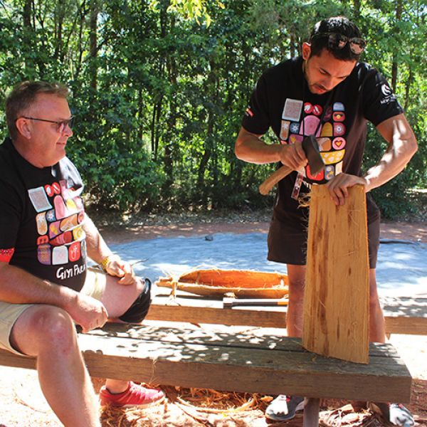 Two men work on building a canoe