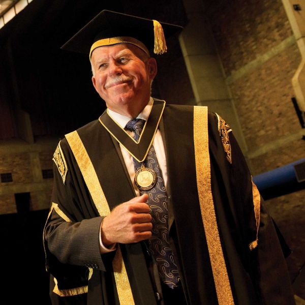Man in ceremonial graduation robes smiling at camera. Farewell from the Chancellor