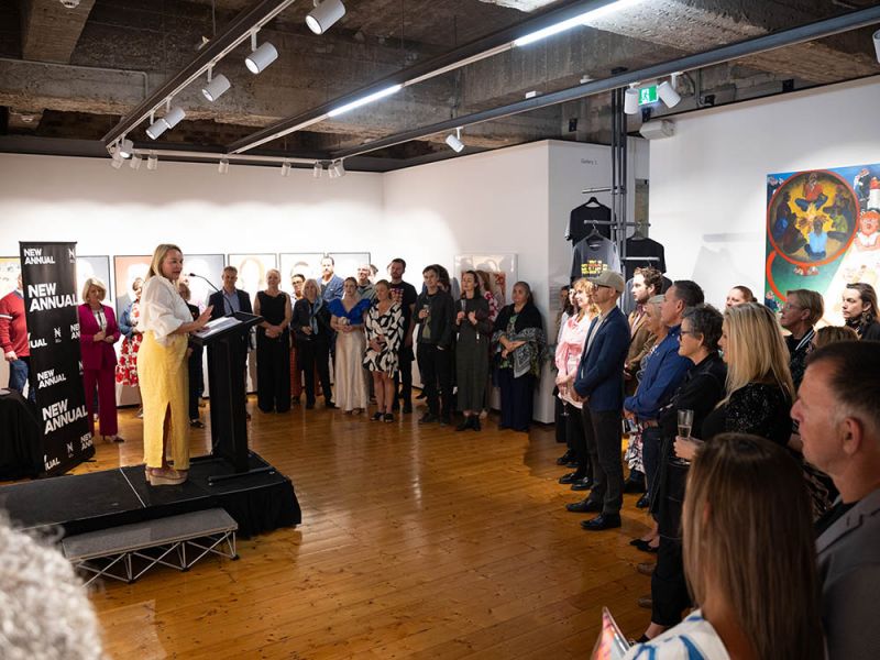 Woman on stage addressing a group of people in an artspace