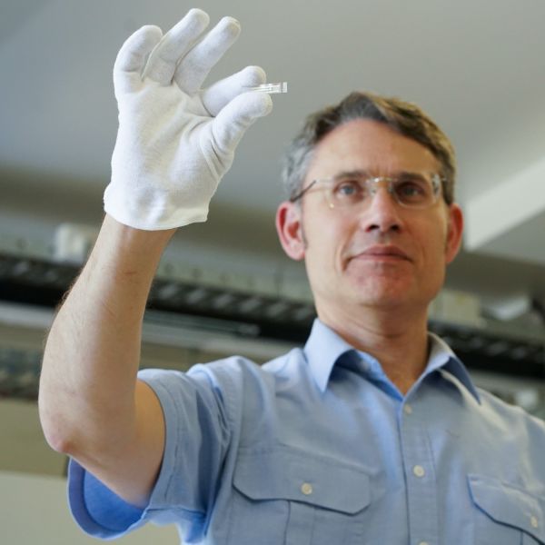 Professor Paul Dastoor in a lab wearing a white glove. In focus in the forefront, he holds the small, transparent biosensor strip
