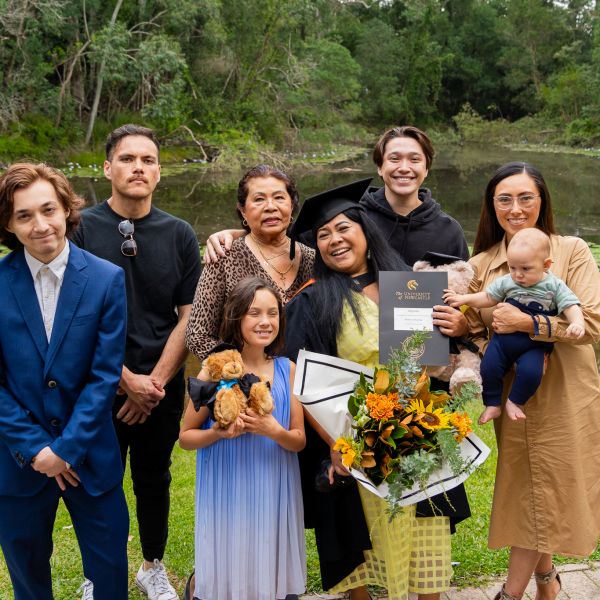 Graduate surrounded by their family near a pond. Proving age is just a number, Arlyn wants to inspire more women in their 50s to pursue education