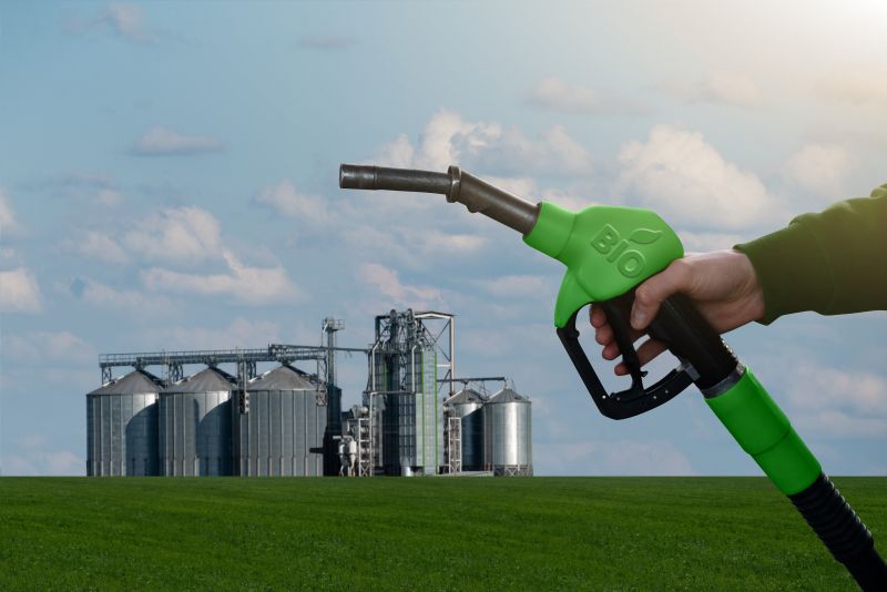 Hand with fuel nozzle with inscription BIO, farming silos in the background