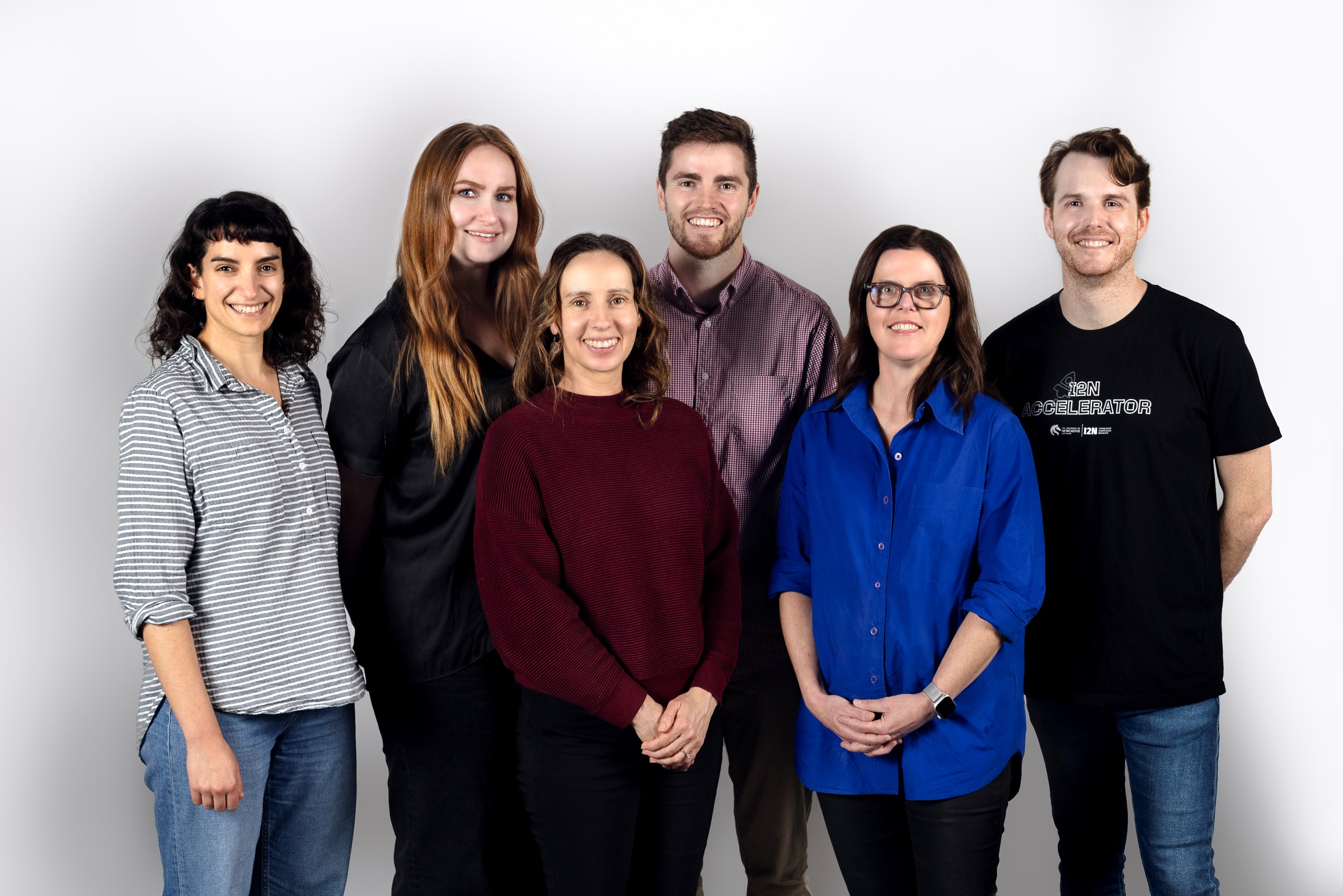 A group of six people smile and pose in front of a white background