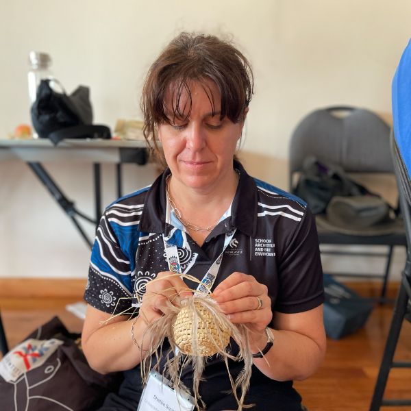 PhD student Shellie Smith sitting on the floor weaving a circle with feathers and straw.