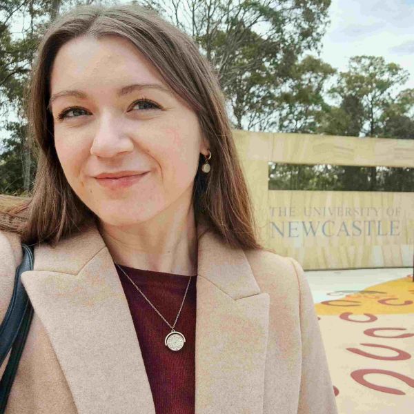 Kristen Troy Kristen standing in front of University of Newcastle sign, grinning