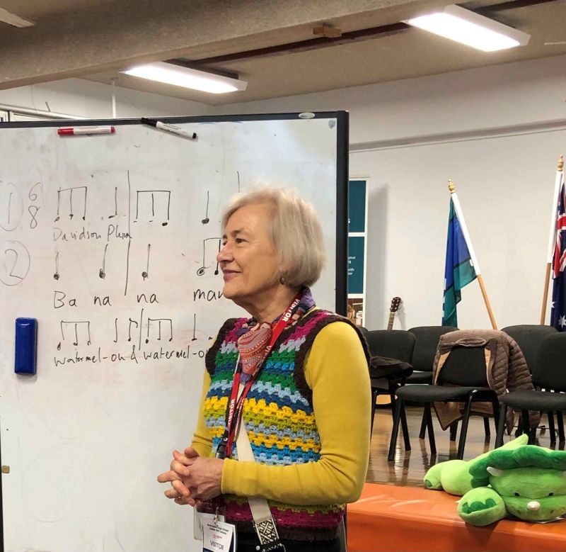 Smiling older woman standing in front of a white board with music notation