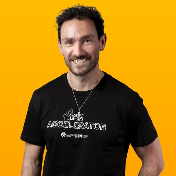 Man wearing a black t-shirt, smiling for the camera in front of a yellow background