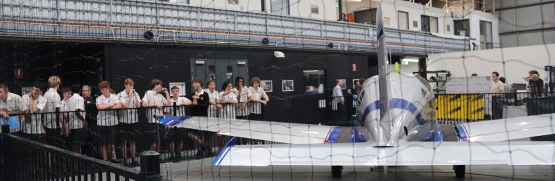 Student stand along a fence, looking at a small plane