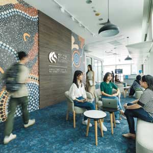 Image of students walking in a colourful corridor of a building in Singapore decorated with Aboriginal and Torres Strait Islander artwork and a University of Newcastle logo