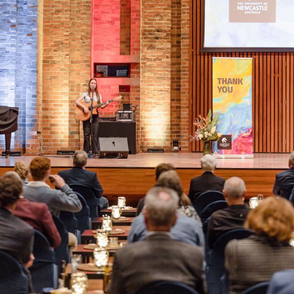 Student with guitar on stage in front of crowd at the Great Hall