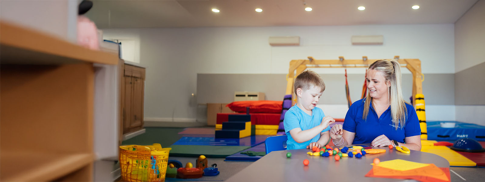 A woman helping a child on a padded floor