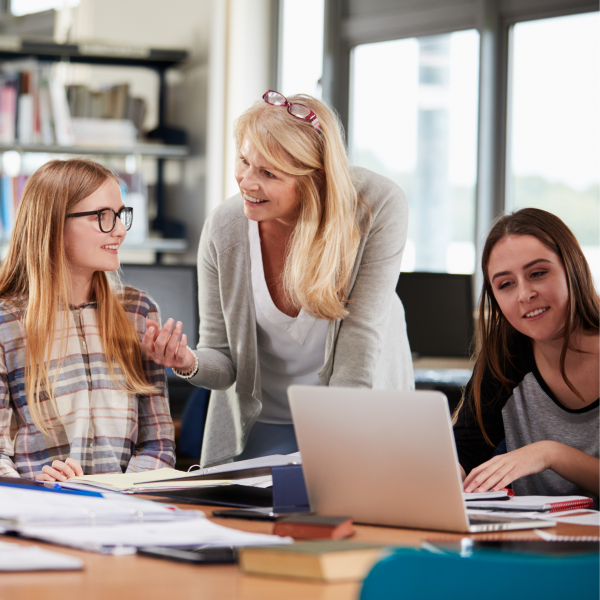 Educator stands in between two students learning at a desk - Quality Teaching in Higher Education