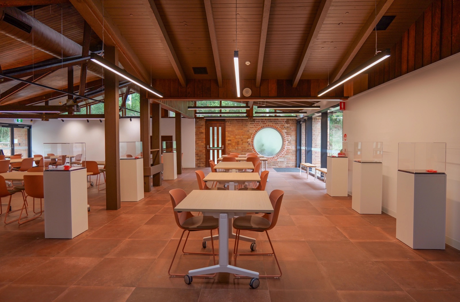 A room with chairs, tables and plinths, and a circular window in warm natural colours.