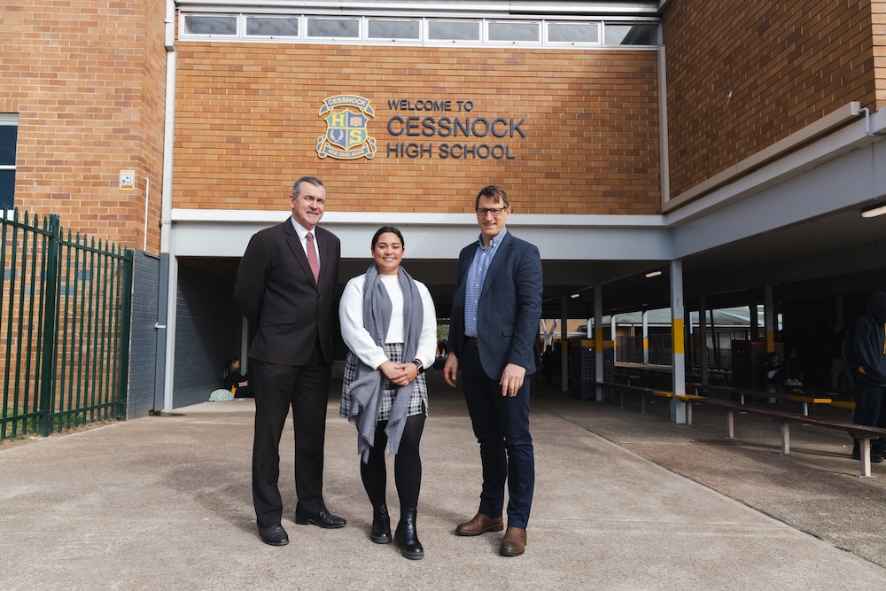 Cessnock High School Principal and teacher standing with Dr Drew Miller outside under school signage