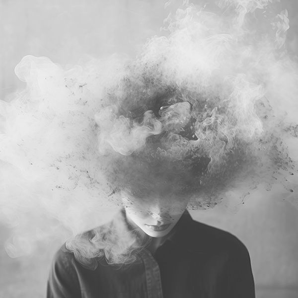 Black-and-white portrait of a person partially obscured by swirling smoke and abstract cloud-like forms that envelop the head and face.
