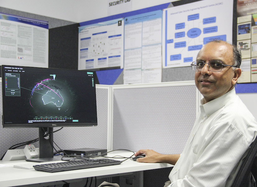 Professor Vijay Varadharajan smiling in front of computer