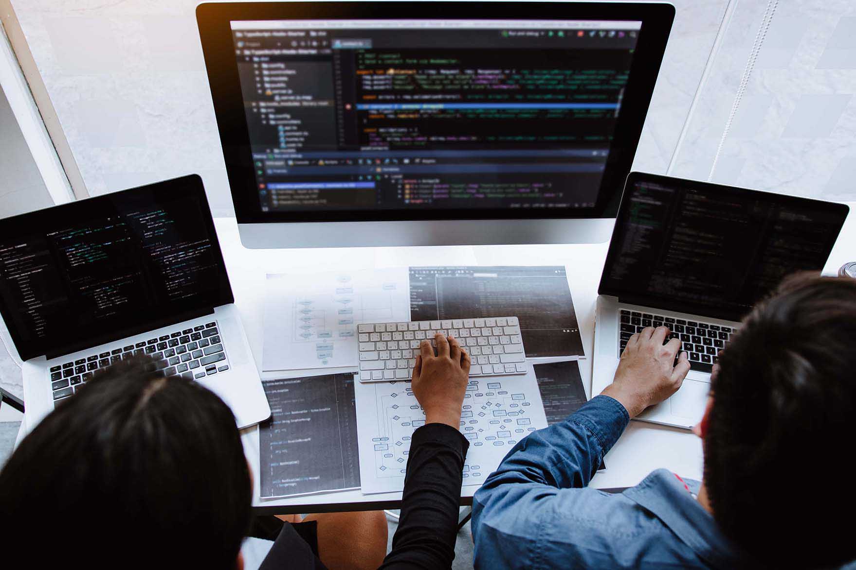 Two people working across three computers