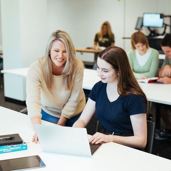 Two women sitting at a desk smiling and looking at a laptop. University of Newcastle receives $479,000 in funding for Women in STEM program