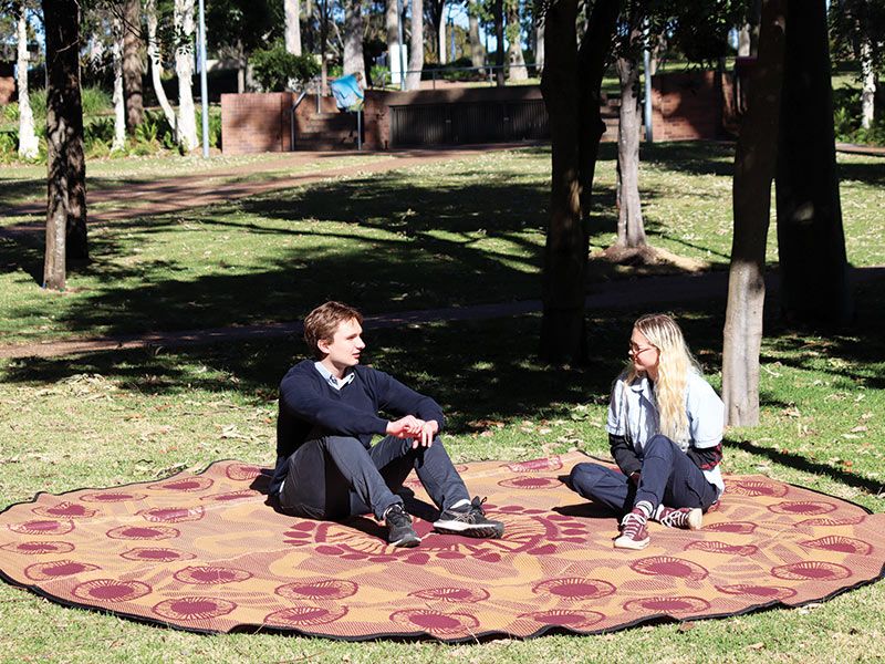 Two people sitting on a Yarning mat having a discussion.