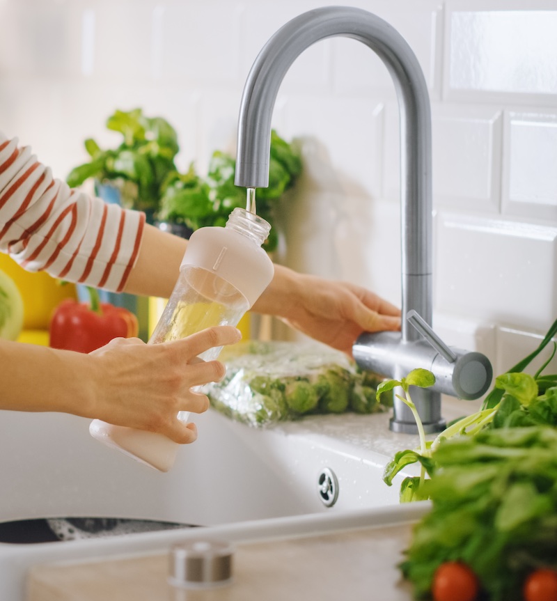 Female filling up an empty water bottle in sink