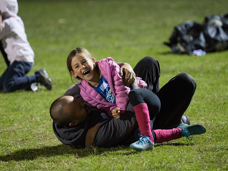 A young girl in a pink coat wrestles her father smiling on the ground