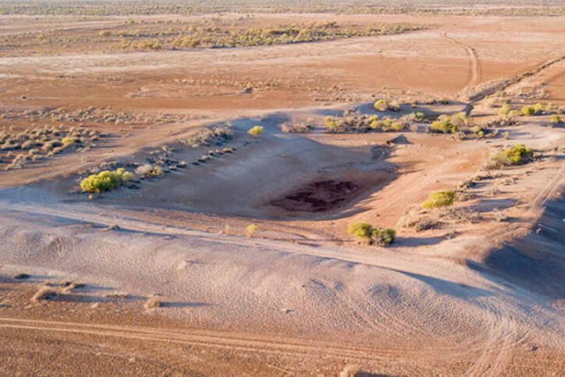 brown dust coats a hollow dam with trees sparsely surrounding the water-less cavity