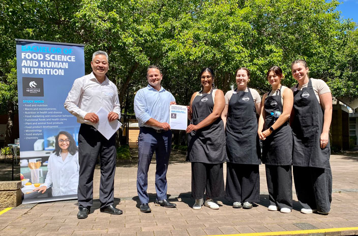 Academic staff stand presenting a certificate to a team of four who have won the competition