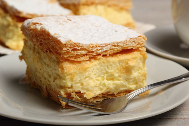 A kremowka, Polish version of a vanilla slice, sitting on a small white plate with a fork beside it