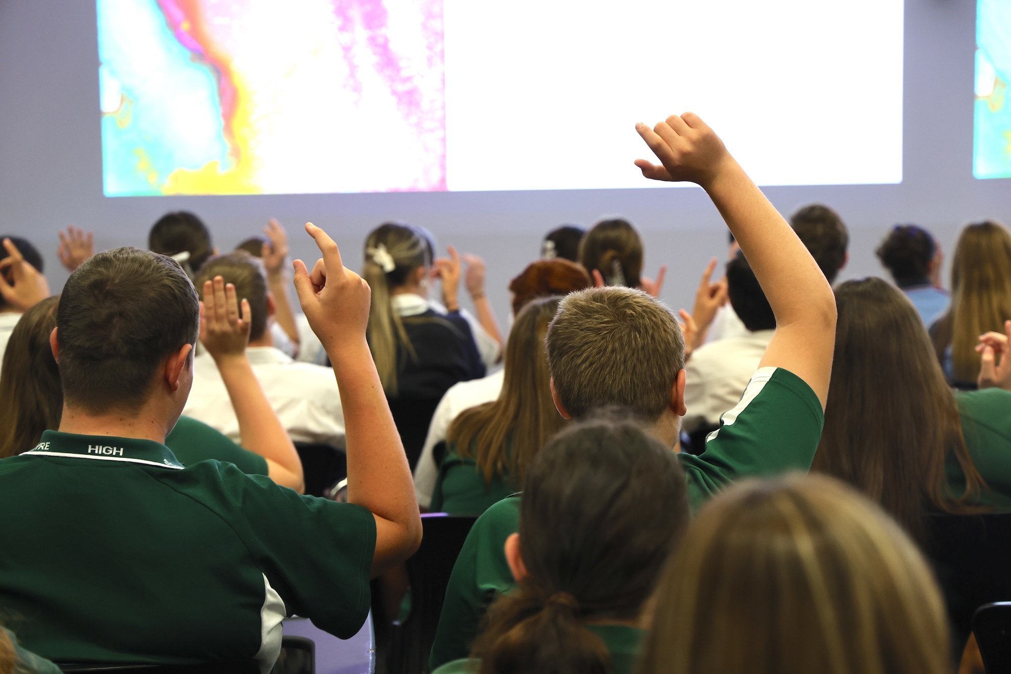 High school students in lecture hall raising hands